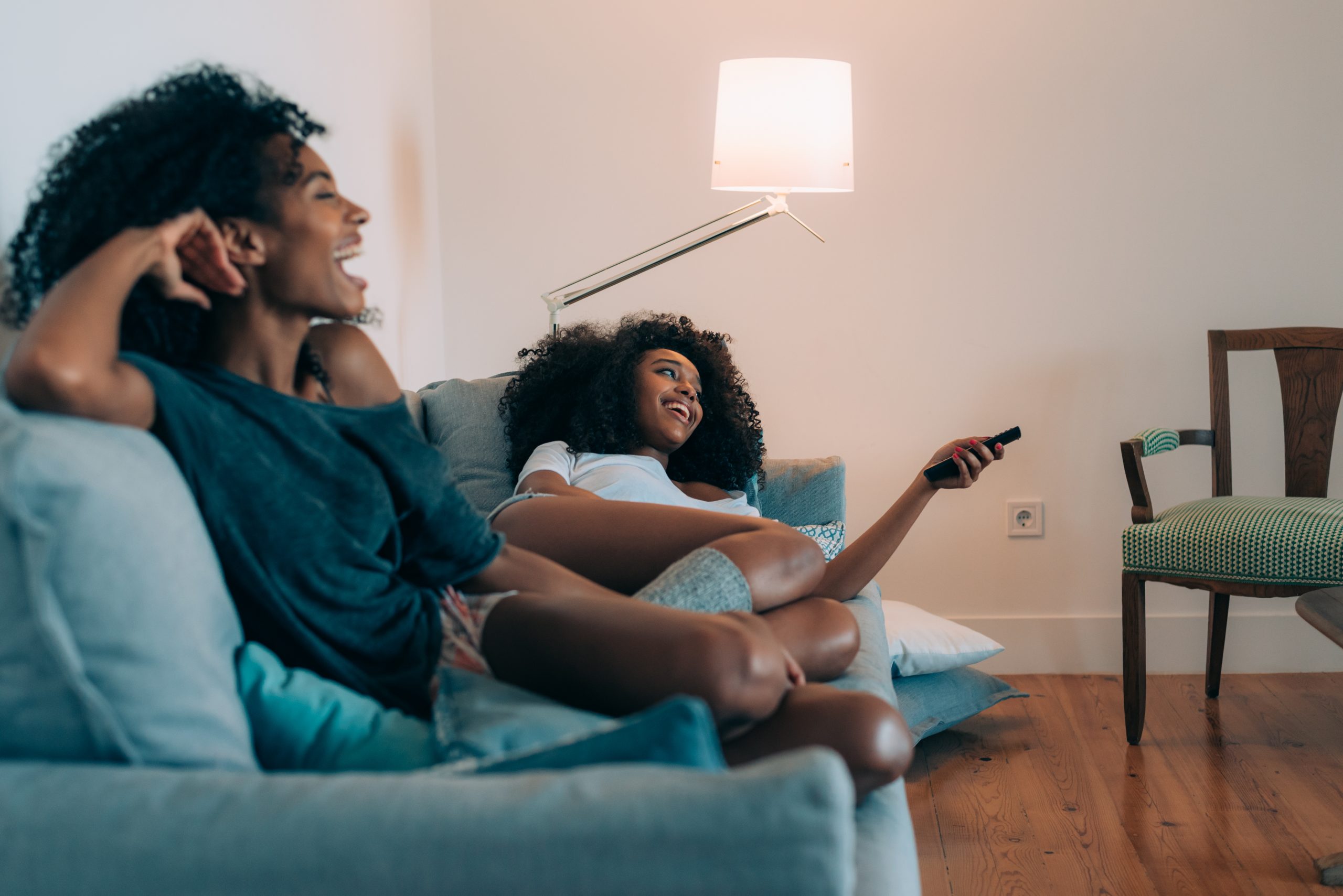 Happy young two black womQen lying down in the couch watching tv