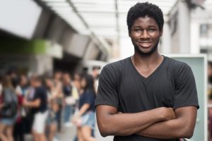 homme africain heureux ; portrait d'un jeune adulte africain à la peau noire, souriant et confiant, en tenue décontractée, scène urbaine en plein air ; modèle d'un jeune adulte ouest-africain