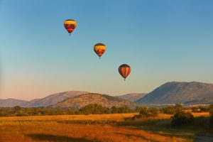 Montgolfières avec touristes au-dessus de la réserve de Pilanesberg. Trois montgolfières décorées de motifs safari sur fond de ciel bleu et de montagnes. Safari de vacances en Afrique du Sud.