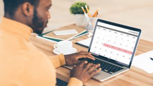 Homme d'affaires noir consultant son calendrier sur son ordinateur portable au travail, planifiant son emploi du temps, collage
