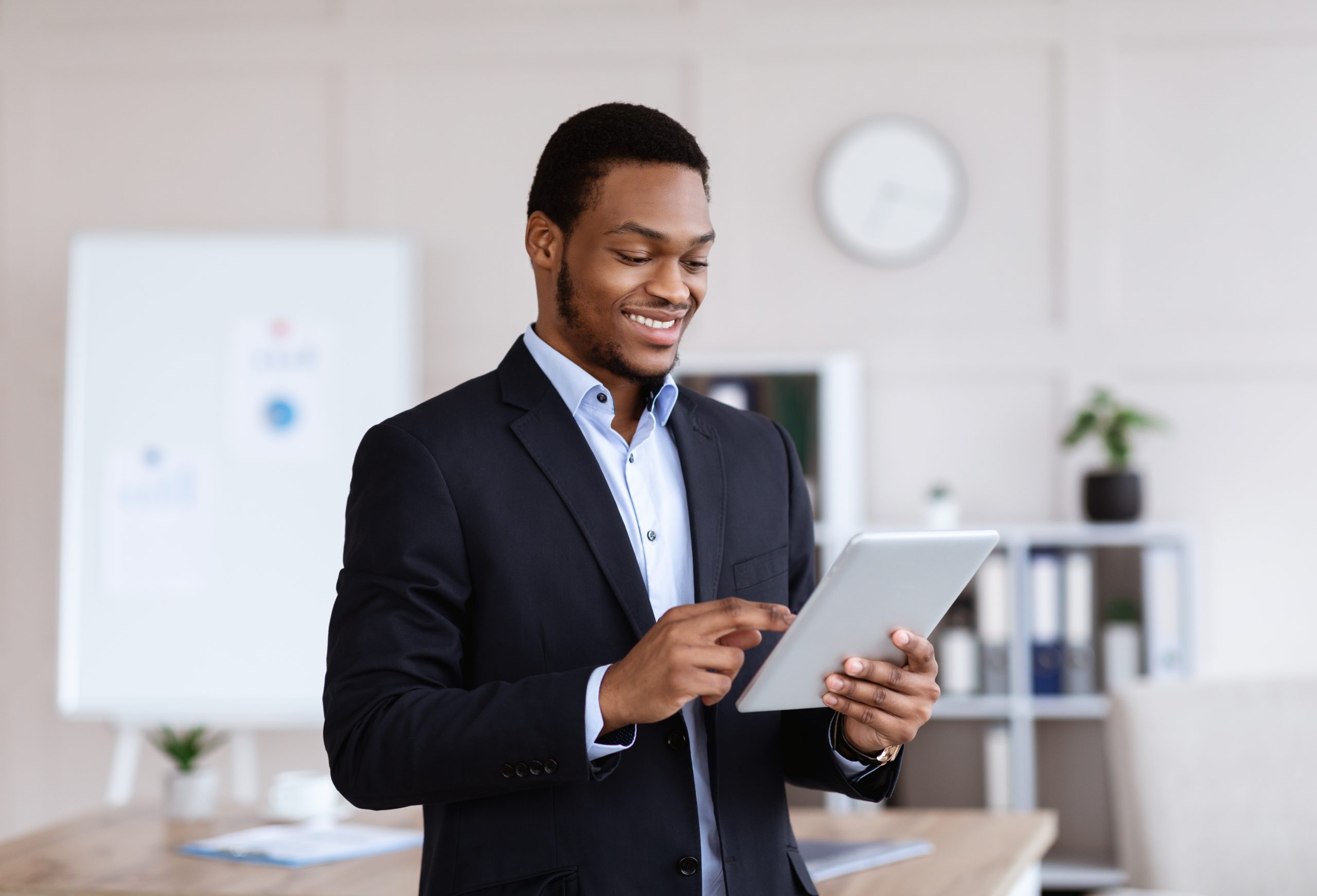 Technologies in business. Happy african american young businessman in black suit using digital tablet in office, working online, reading marketing report, getting ready for presentation, copy space