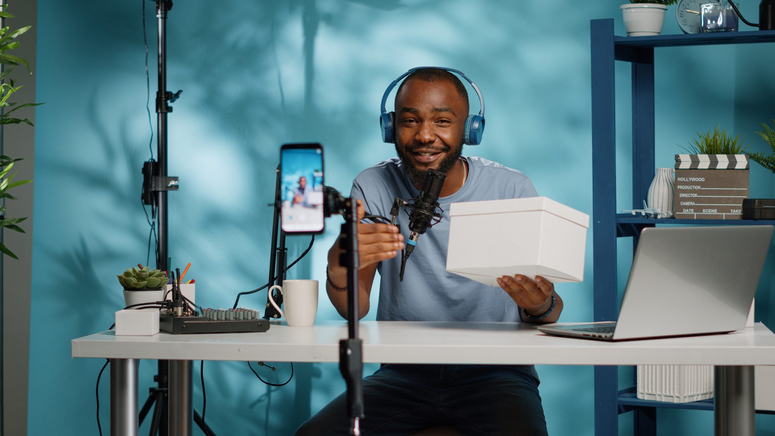 Black blogger doing giveaway contest and recording video for channel. African american influencer holding present box to give to subscribers on camera, filming on smartphone for vlog.