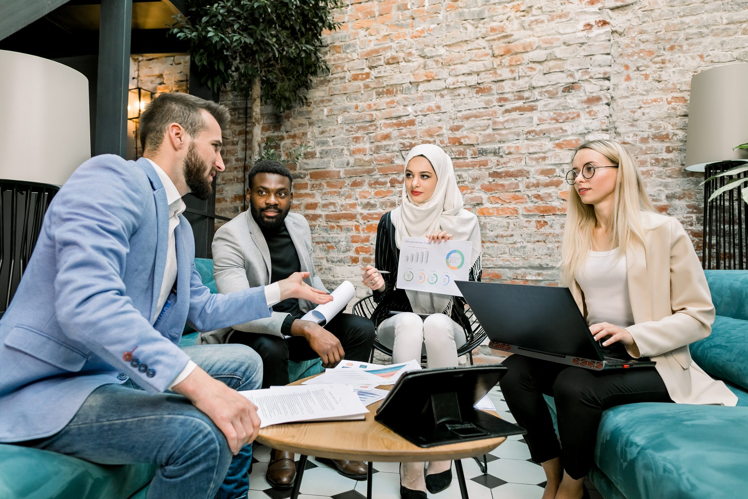 Multiethnic business people on the meeting in office. Arabian business lady in white hijab using financial document with graphs talking to her male and female partners about the results of research.