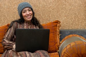 Belle jeune femme arabe utilisant un ordinateur portable et souriant à la caméra et assise dans un salon marocain
