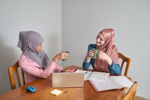 Two muslim business women wearing hijab working in a laptop and drinking coffee.