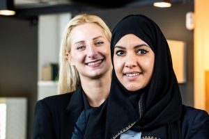 Femmes d'affaires souriantes de différentes ethnies et cultures regardant la caméra dans un bureau moderne - Deux amies élégantes, l'une d'elles portant un voile hijab islamique typique - Concept de diversité