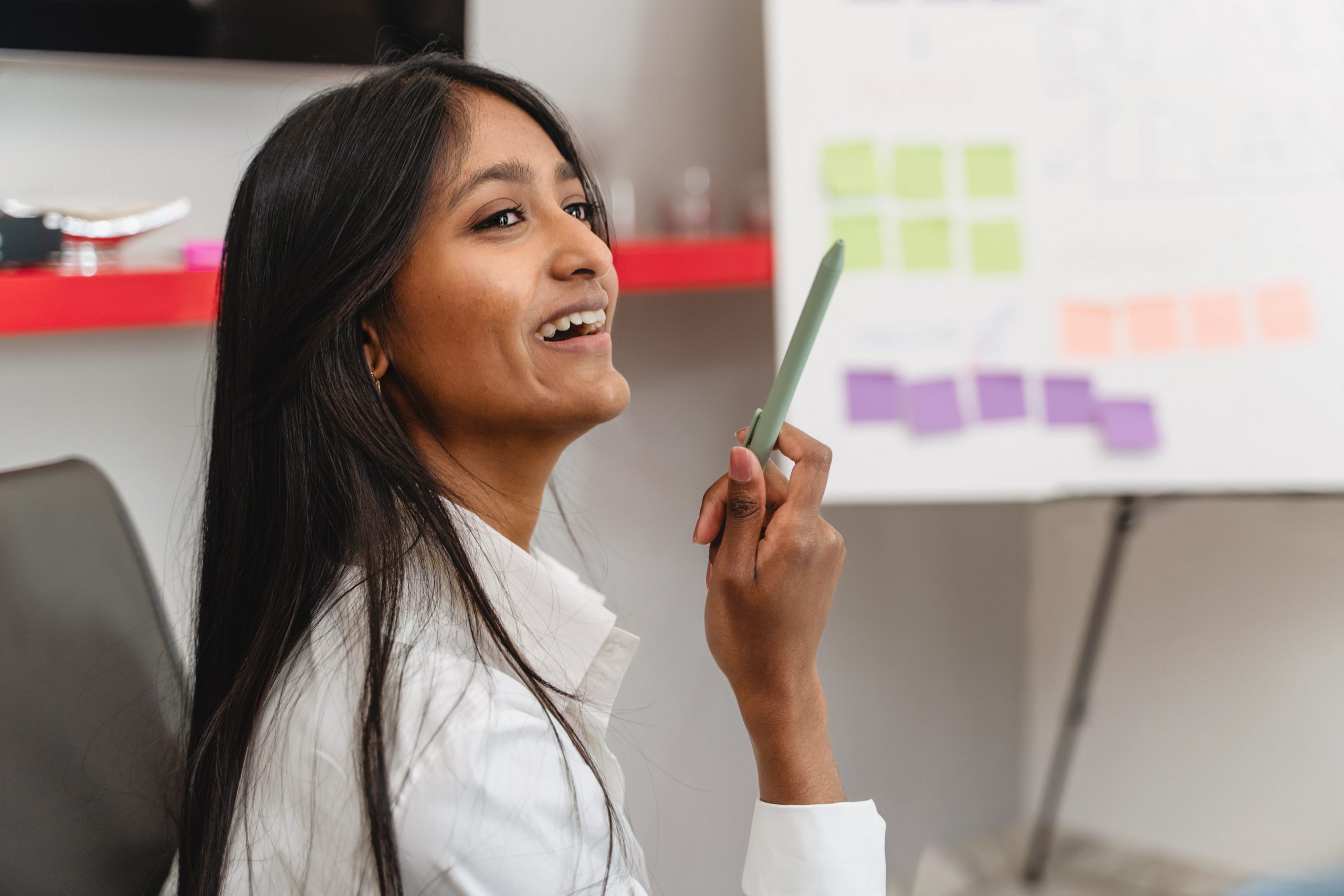 Professional African Asian descent woman leads a business presentation reflecting the innovative ideas to her colleagues, against a whiteboard with colorful sticky notes.